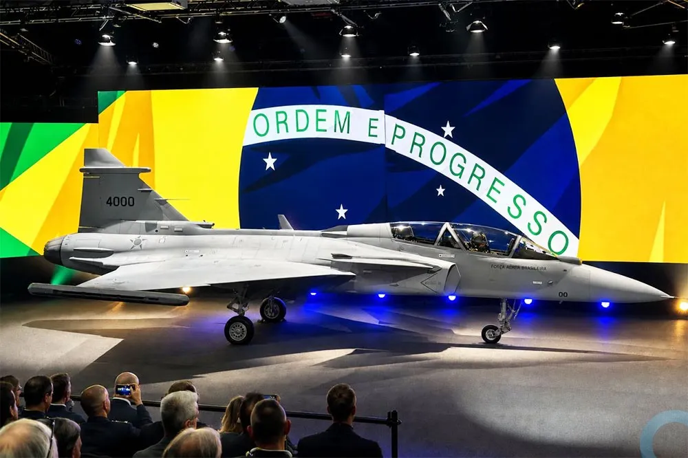 Caça Gripen F da Força Aérea Brasileira é apresentado em evento com bandeira do Brasil ao fundo. (Foto: defesanet.com.br)
