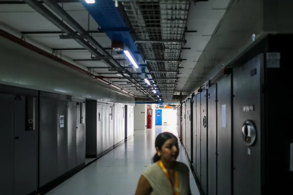 Mulher caminha por corredor de data center com painéis de servidores em ambos os lados. (Foto: techcrunch.com)